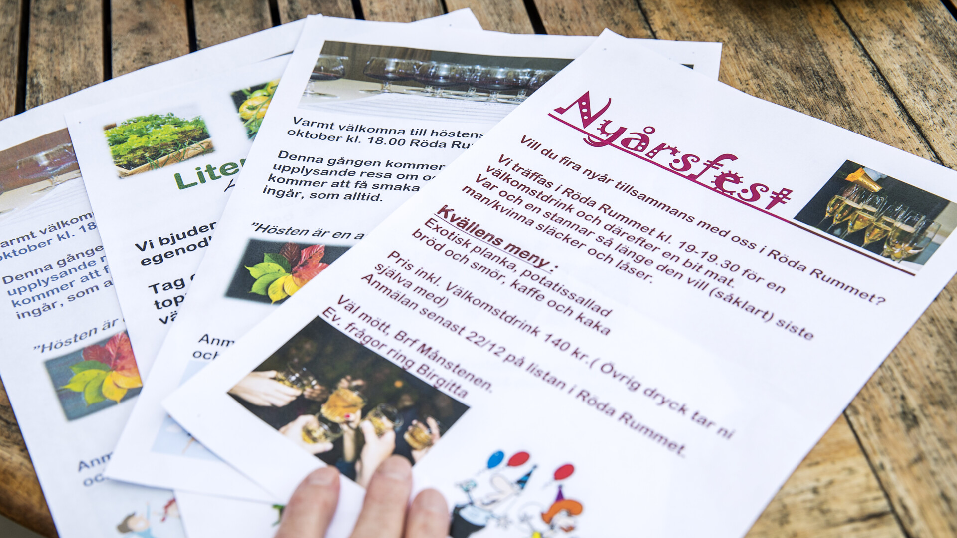 Flygblad och inbjudningar liggande på ett träbord, med text om höstfest och bilder på mat och dryck