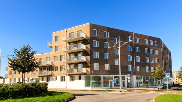 Modernt flerbostadshus med balkonger och butikslokaler i bottenvåningen, mot klarblå himmel