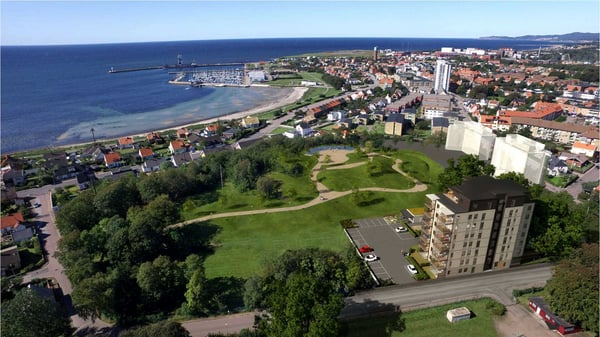 Flygvy över kuststad med grönområde, småhus och flerbostadshus nära havet