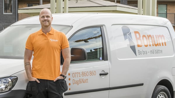 Man i orange Bonum-pikétröja står framför en vit servicebil med Bonum-logotyp