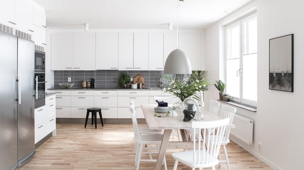 Lägenhet med modernt vitt kök, matplats och stora fönster i ett ljust rum