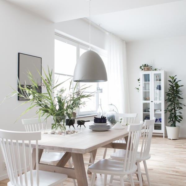 Ljusa vita stolar runt ett matbord i en modern och ljus matplats med stora fönster och gröna växter