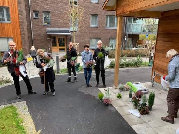 Flera personer håller växter och blommor på en gårdsplan vid ett bostadshus