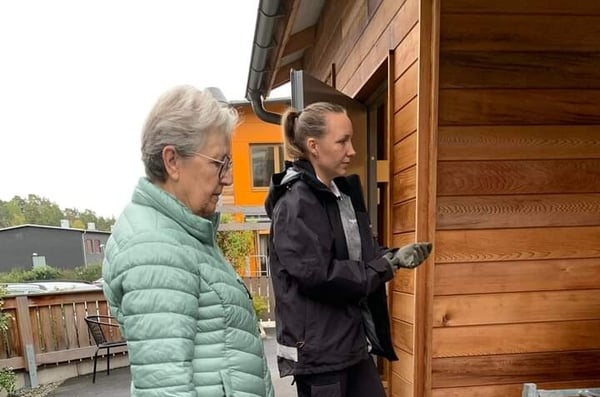 Två kvinnor utanför ett trähus, varav en öppnar en dörr