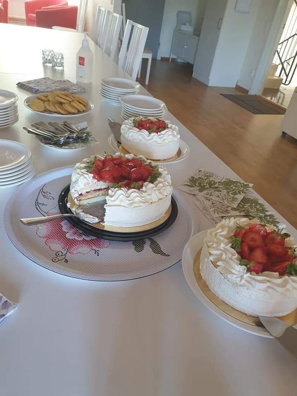 Fikabord med flera jordgubbstårtor, kakor och porslin i en ljus matsal