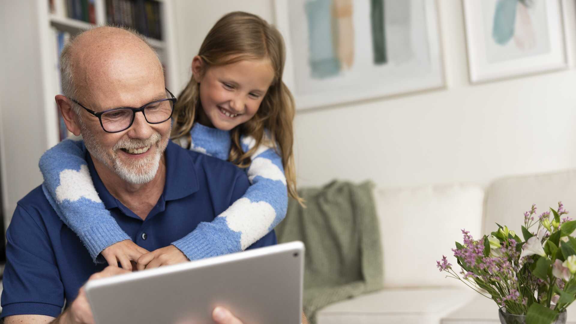 Man tittar på ipad med barnbarn i soffa